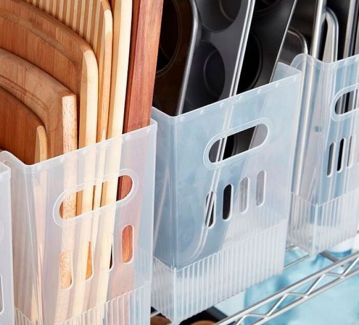 Uma solução simples e acessível para quem busca otimizar espaços em armários ou prateleiras de cozinhas compactas, mantendo o visual limpo e funcional. Caixas plásticas organizando tábuas e formas em uma prateleira.