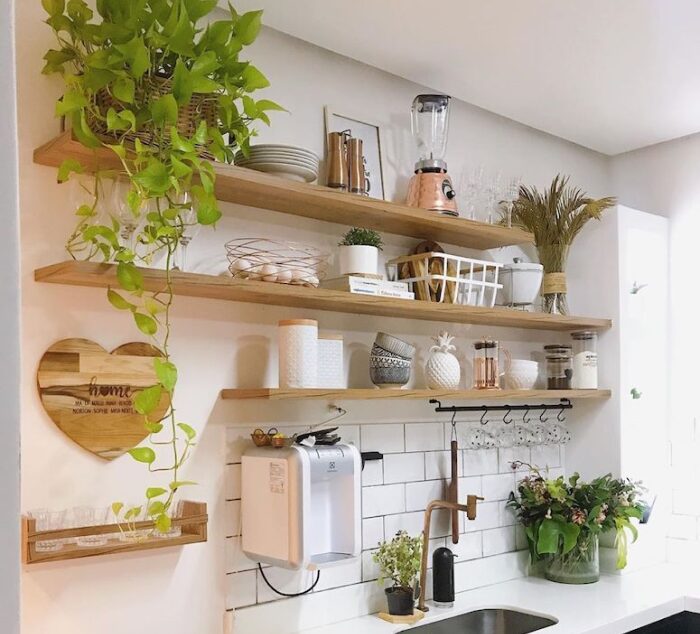 Exemplo de como unir organização e estilo em uma cozinha pequena, usando prateleiras abertas, objetos decorativos e vegetação para trazer charme e praticidade. Cozinha compacta decorada com prateleiras de madeira, utensílios e plantas.