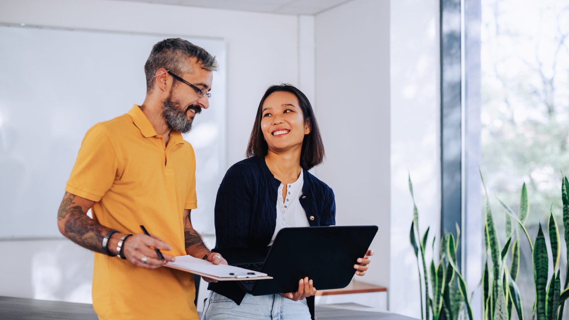 Uma mulher e um homem sorridente usando laptop em casa moderna, representando o início da jornada de compra do primeiro apartamento.