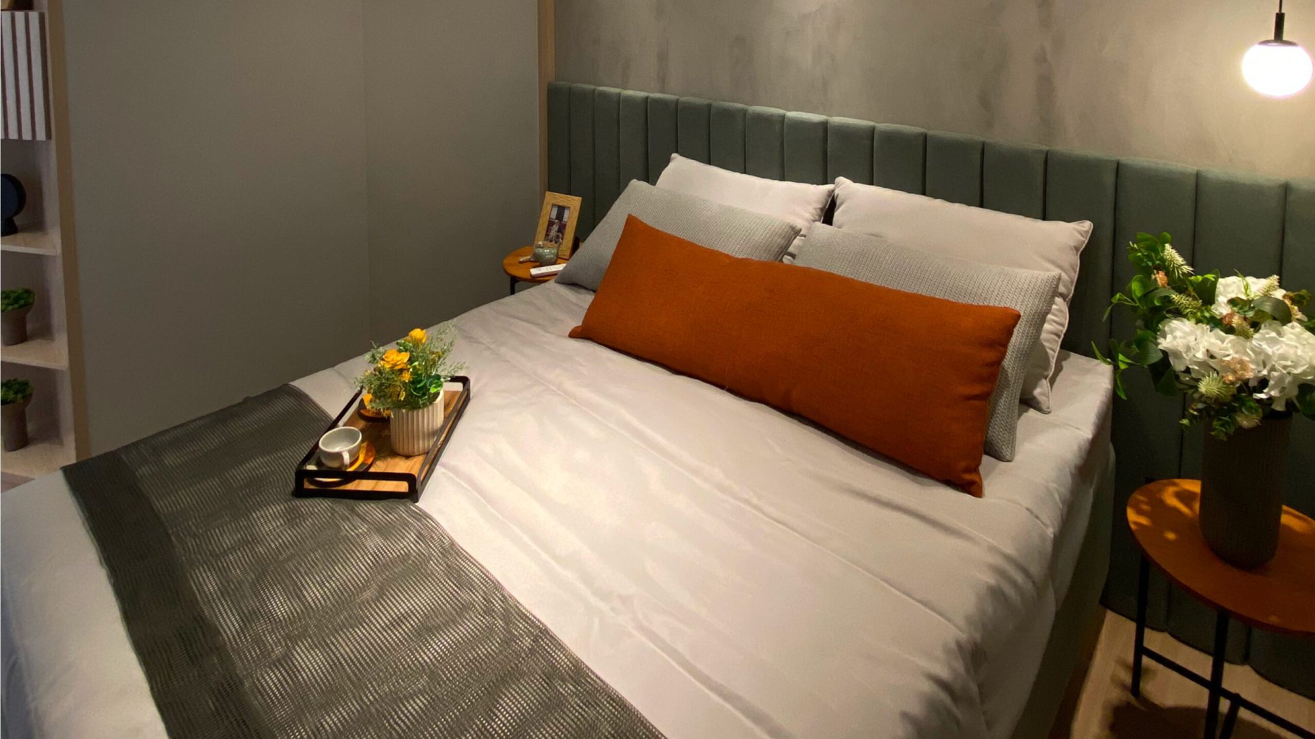 Quarto de casal decorado com tons claros, cama com almofadas decorativas, iluminação suave e elementos minimalistas.