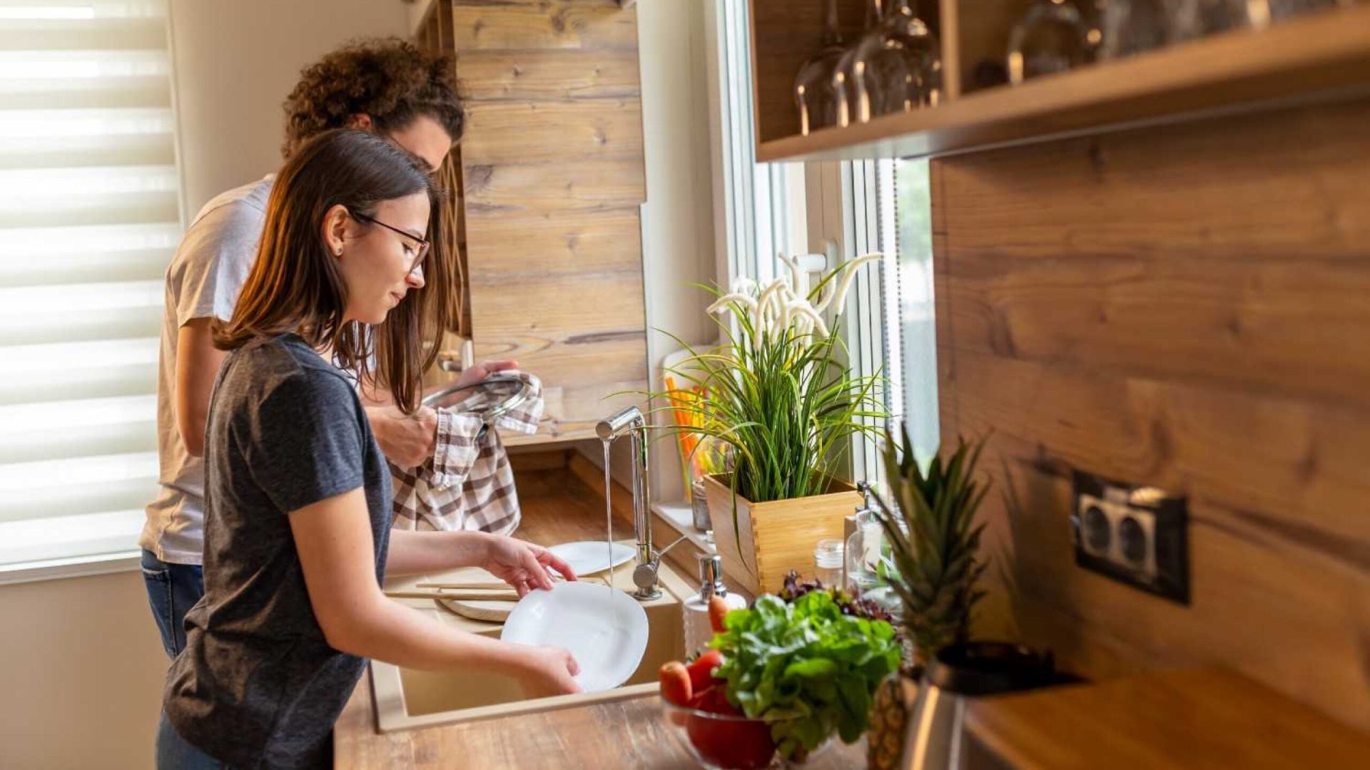 Casal lavando louça em uma cozinha com decoração em madeira.
