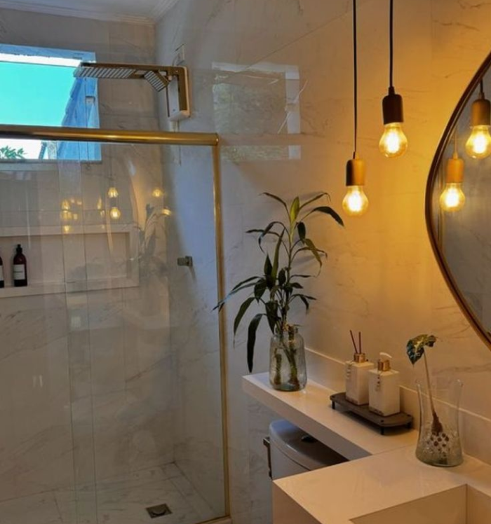 Decoração de bancada de banheiro com elementos naturais e iluminação suave, ideal para criar um clima de bem-estar e leveza. Detalhe de bancada com torneira cromada e vasos decorativos com folhagem verde.